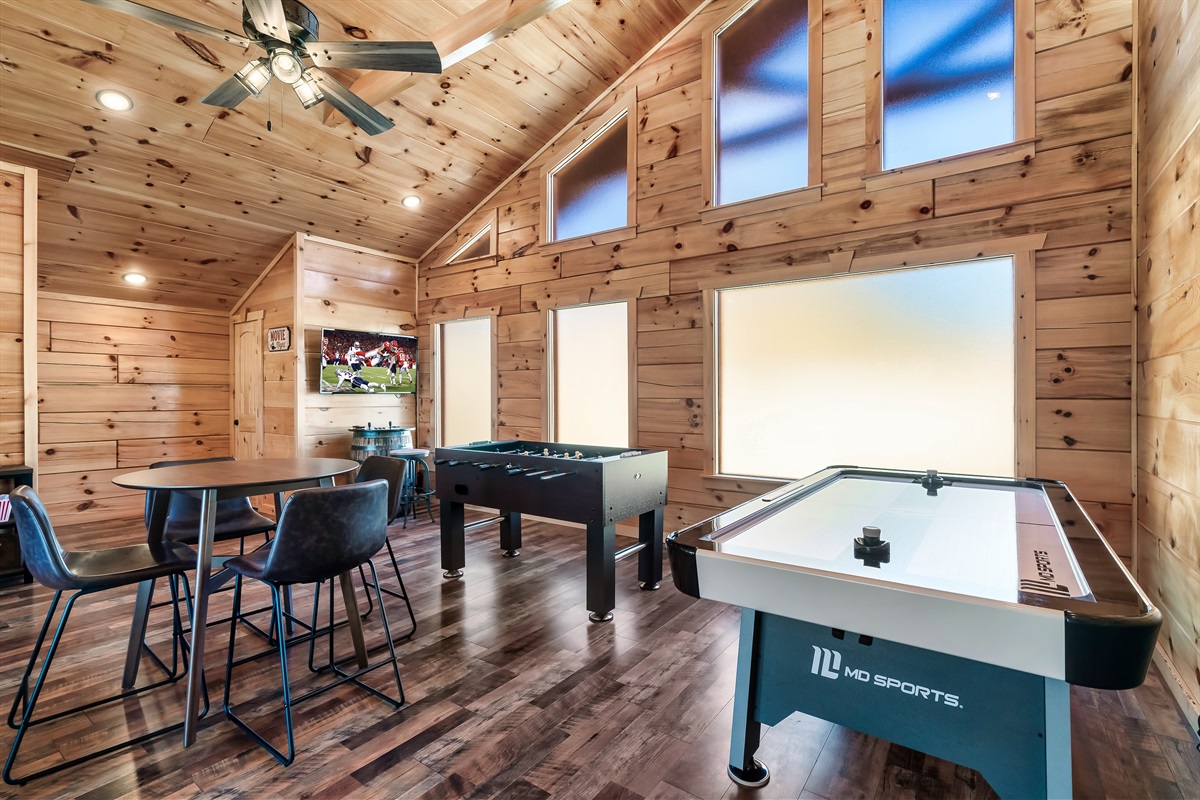 Spacious wood-paneled game room with air hockey, foosball, barrel arcade + smart TV, and high-top cafe seating