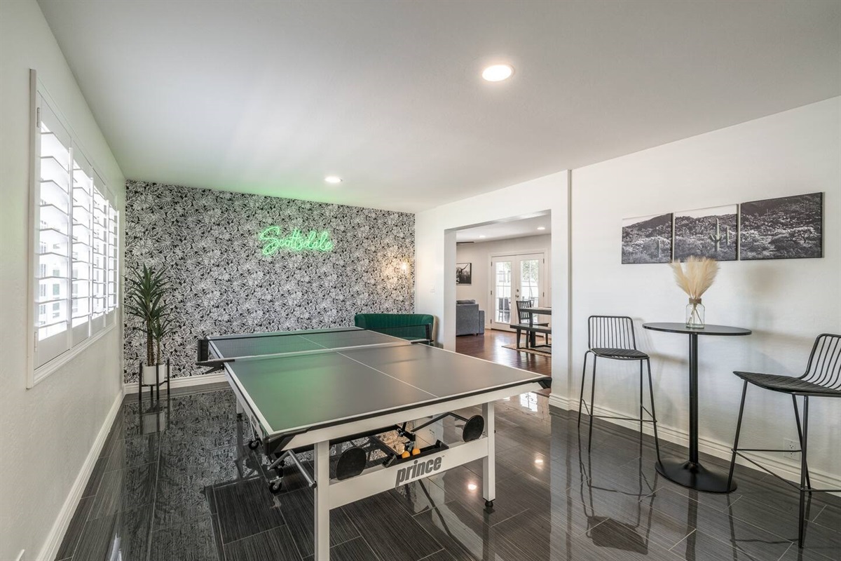 The swanky ping pong room features a super chic vibe with a green velvet love seat, bar-height table, and neon sign.