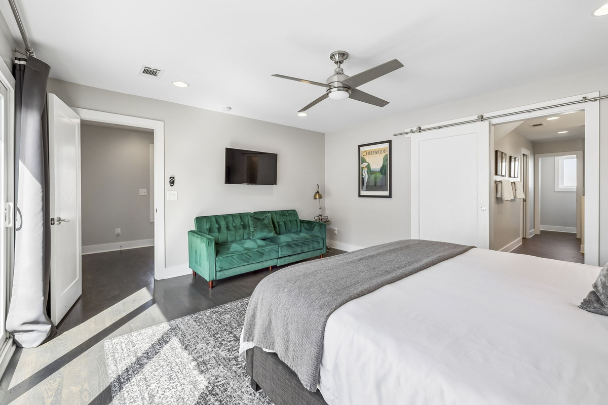Emerald green tufted sofa adds a vibrant pop of color to this spacious bedroom lounge - Wall mounted TV and large windows make this a great spot for relaxing or streaming - Sophisticated black out drapes and detailed rug complete the room&rsquo;s upscale feel