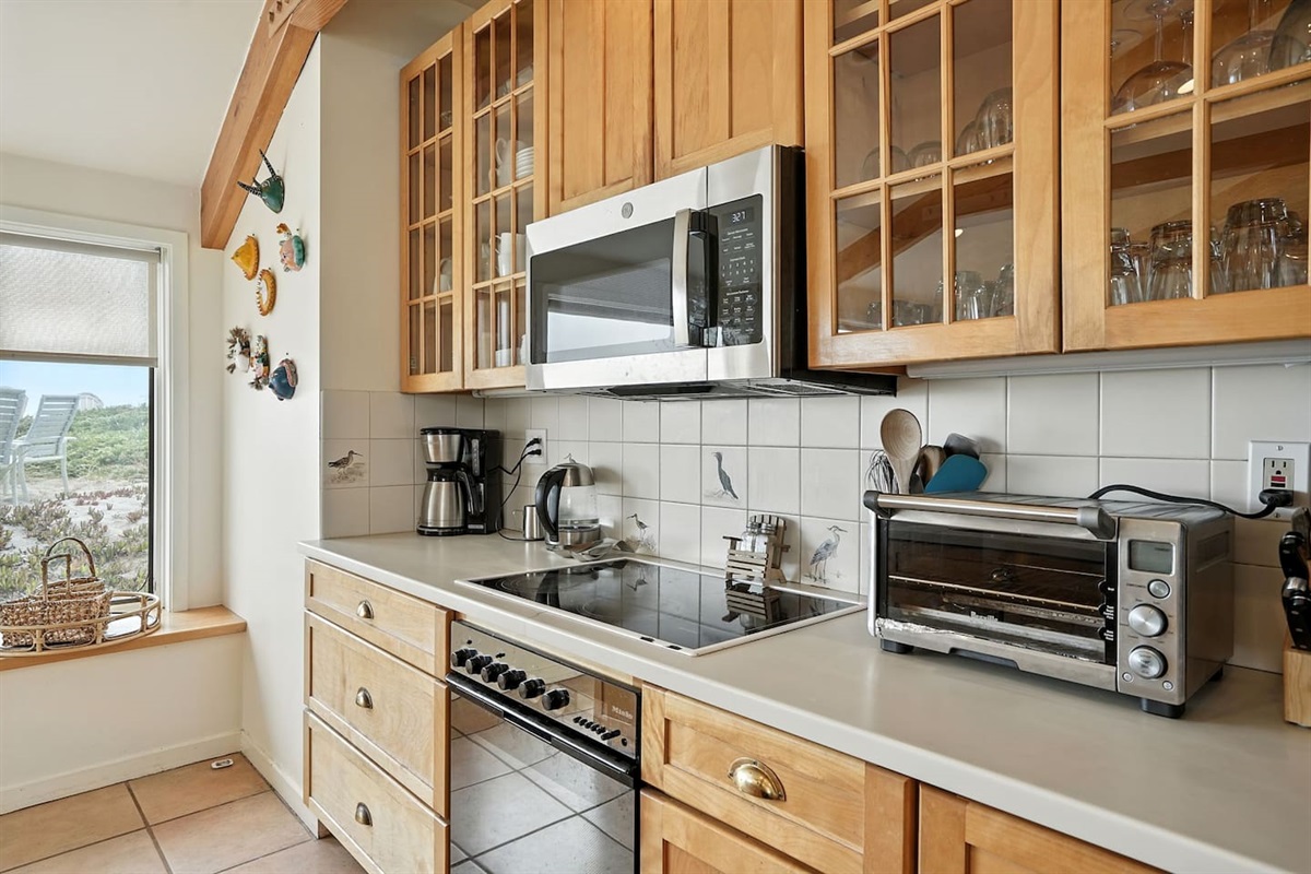 - Bright kitchen with wood cabinetry, large windows & modern appliances for easy cooking  
- Features electric cooktop, microwave, toaster oven & coffee maker for convenience  
- Scenic dune views create a relaxing atmosphere while you prepare meals