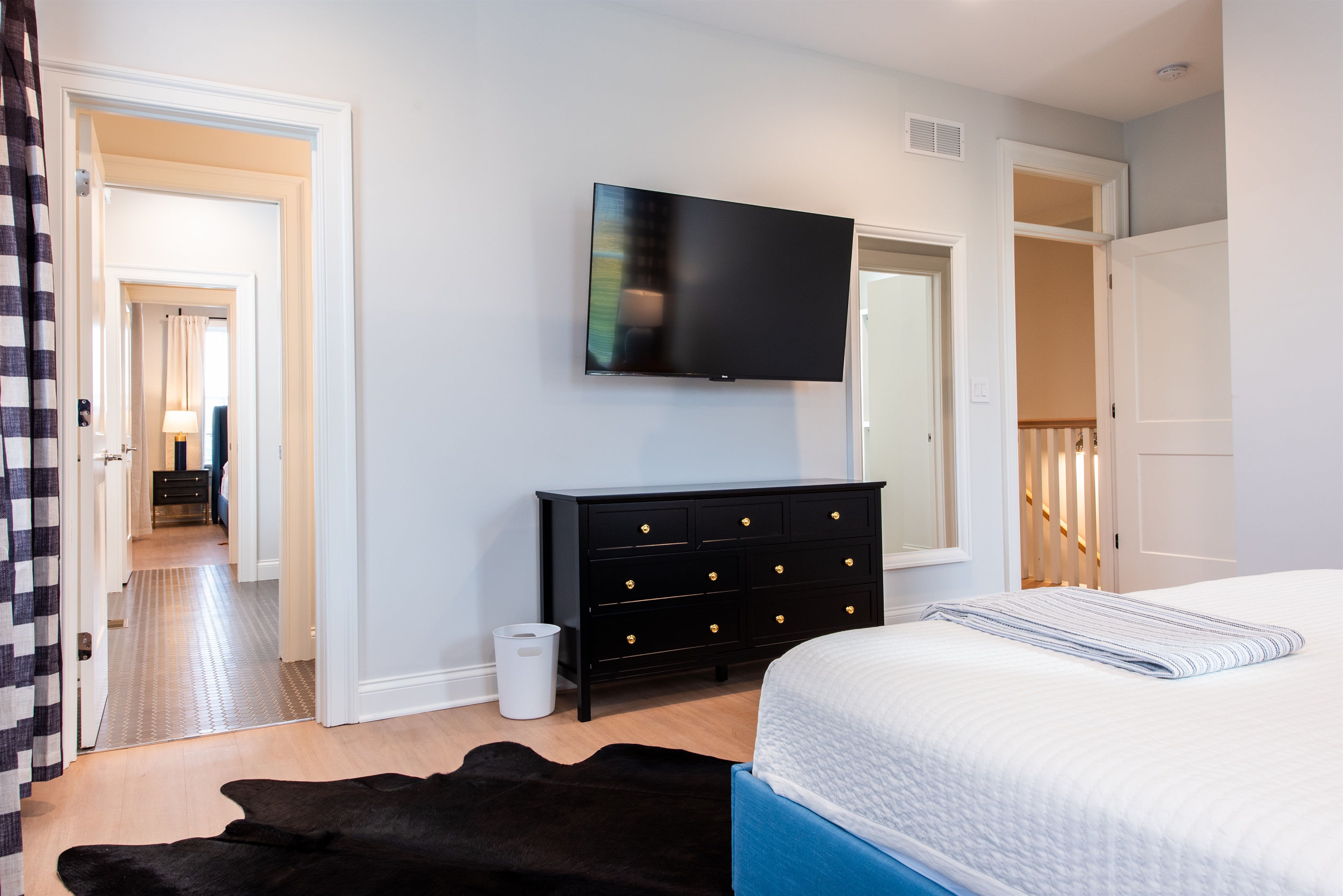 Enjoy this spacious and stylish bedroom with a cozy blue bed, large dresser, and wall-mounted TV for ultimate relaxation. The open layout connects to other rooms, making it an ideal spot for your stay on the Bourbon Trail.