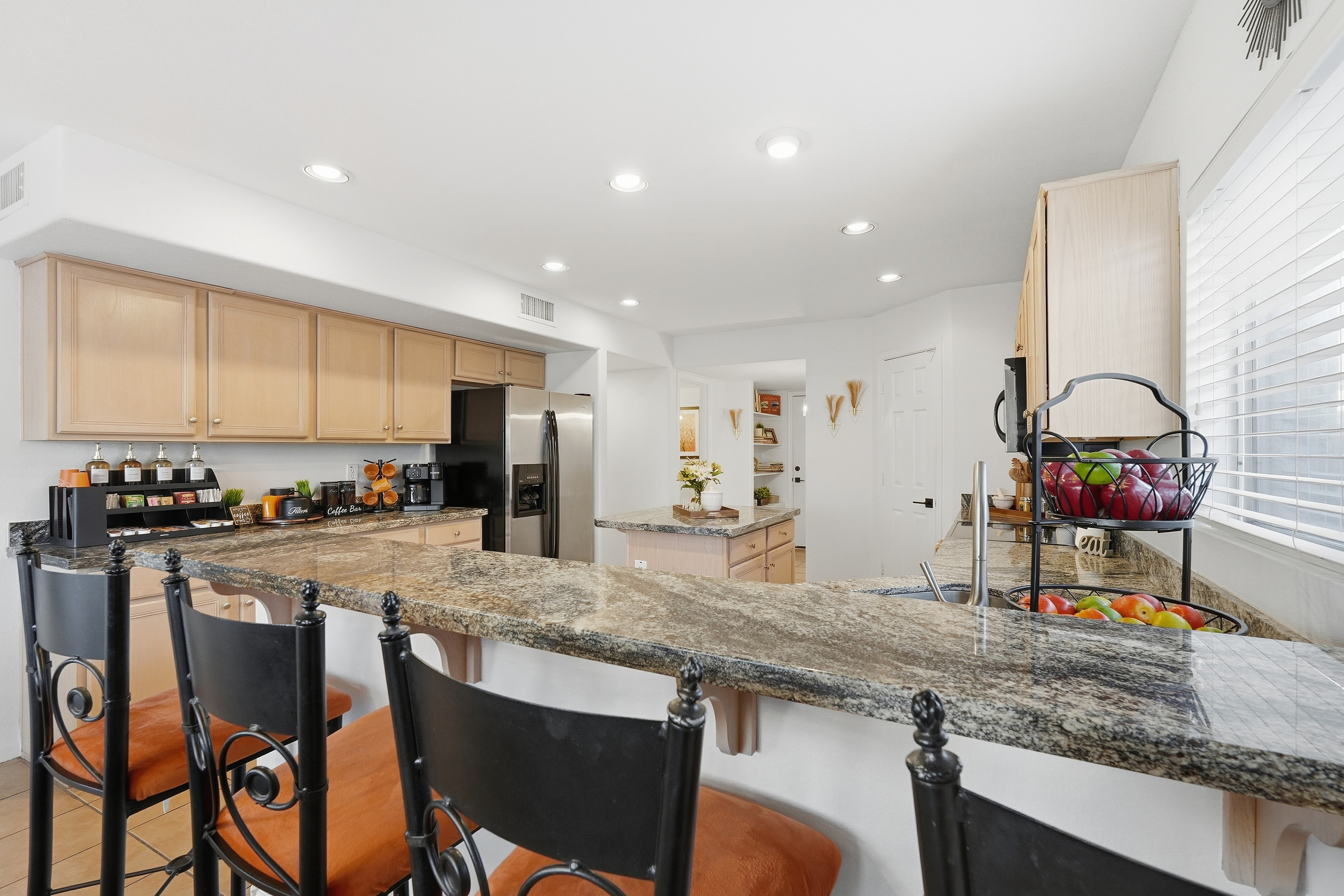 Kitchen breakfast bar with counter seating, granite counters, and open views across the full kitchen and entry area.