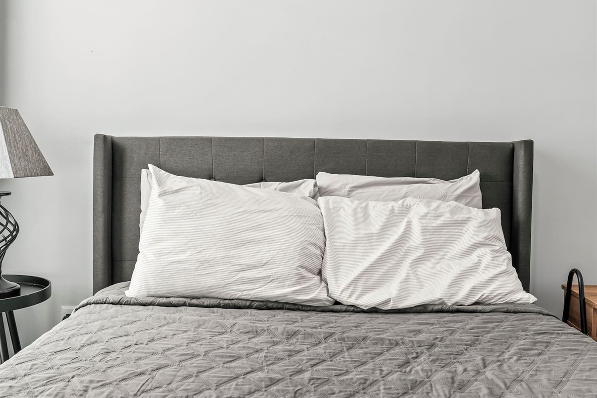 Second bedroom window-side angle with bedside table, lamp, and blackout curtains for restful nights.