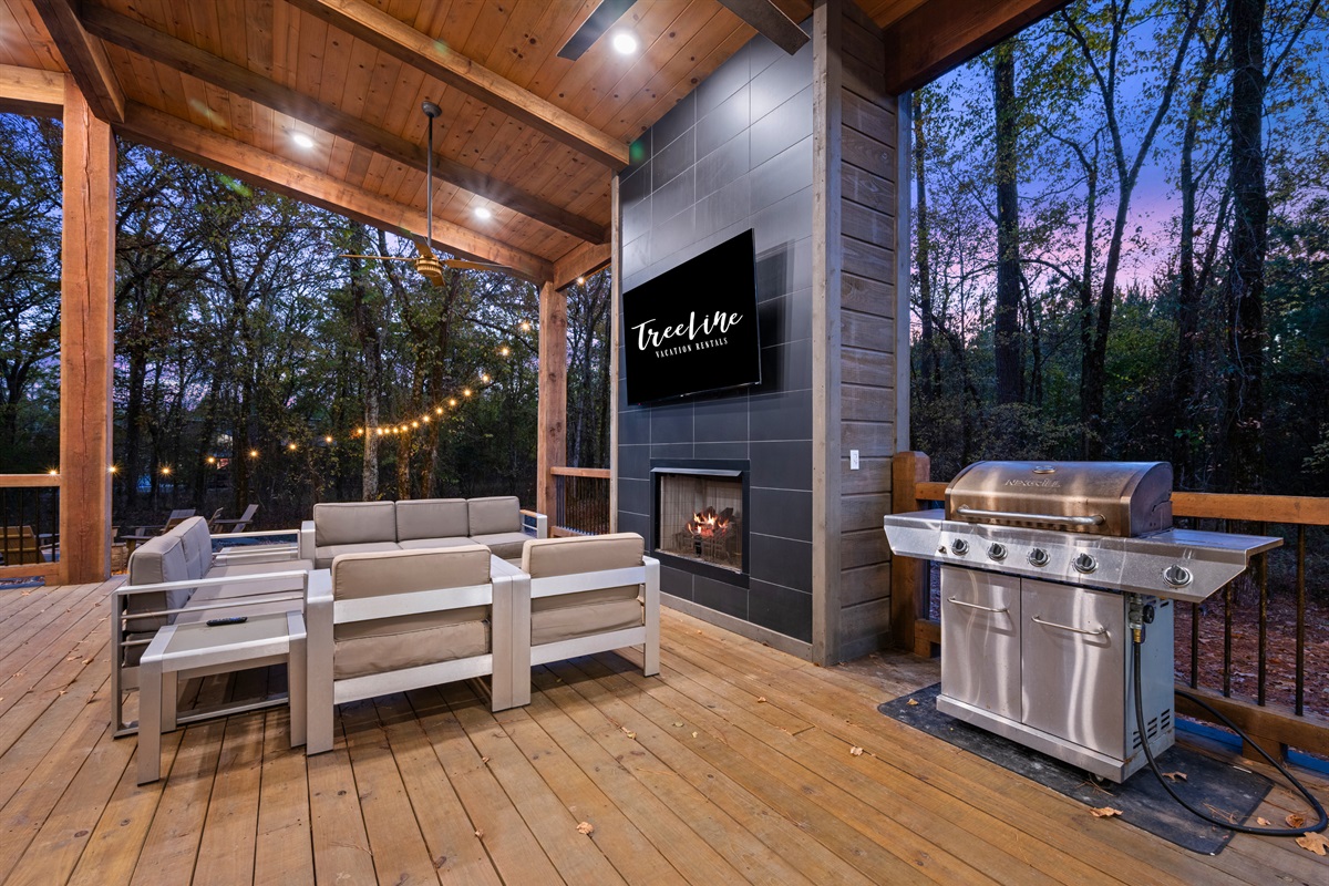 The ultimate outdoor lounge, featuring a fireplace, TV, and comfy seating under a beautiful wooden pavilion.