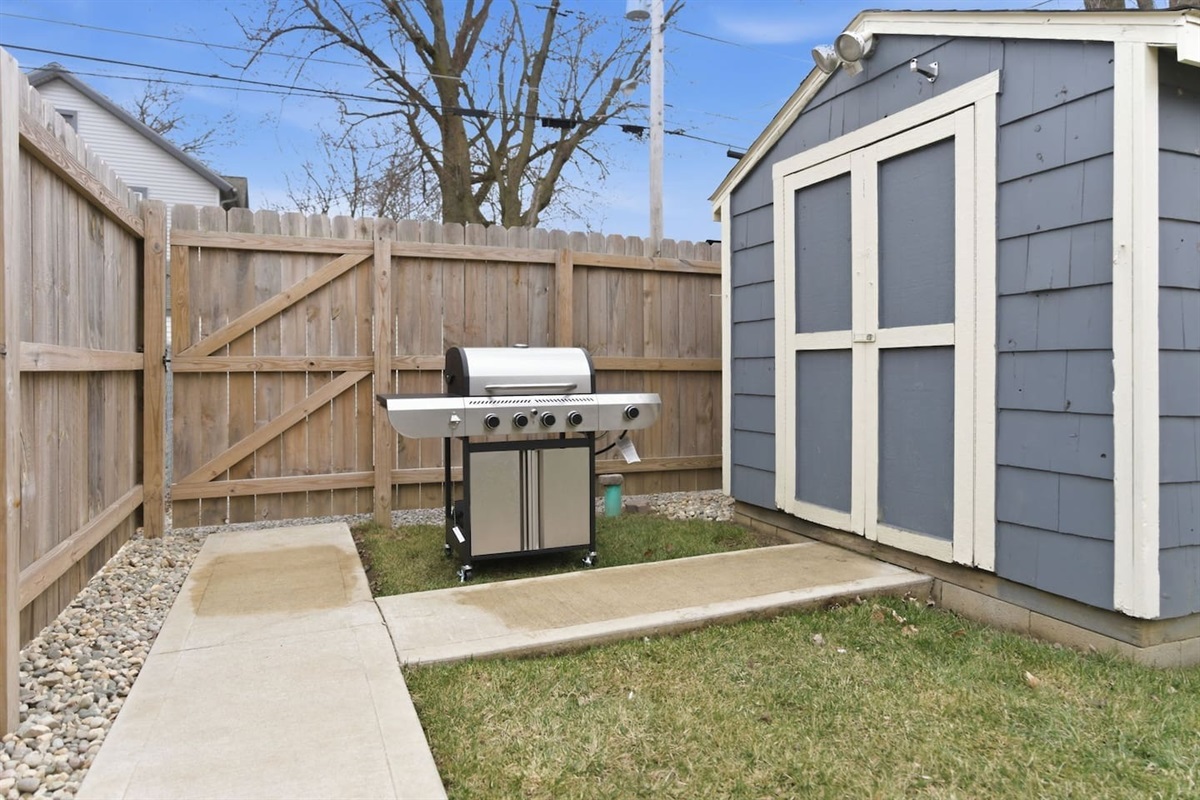 Backyard setup with grill and storage shed, perfect for outdoor cooking and convenience