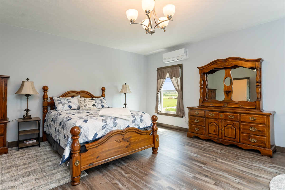 A bright and spacious master bedroom featuring a cozy queen bed, Queen fold out sofa and crib with elegant wood furniture, and stunning countryside views through large windows. Perfect blend of comfort and charm for a restful stay. Bedroom #1
