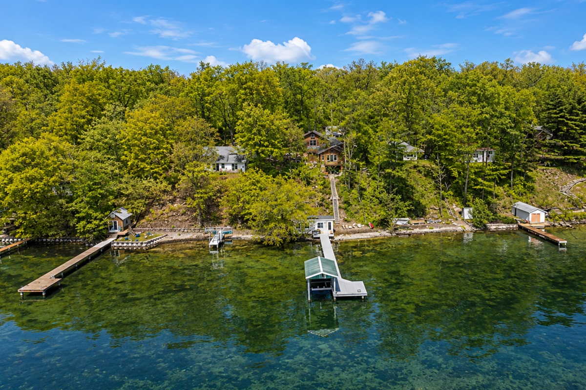 This stunning aerial view highlights a serene lakeside community, showcasing scattered cottages, lush greenery, and extensive docks for easy access to crystal-clear waters. An idyllic retreat for nature lovers.