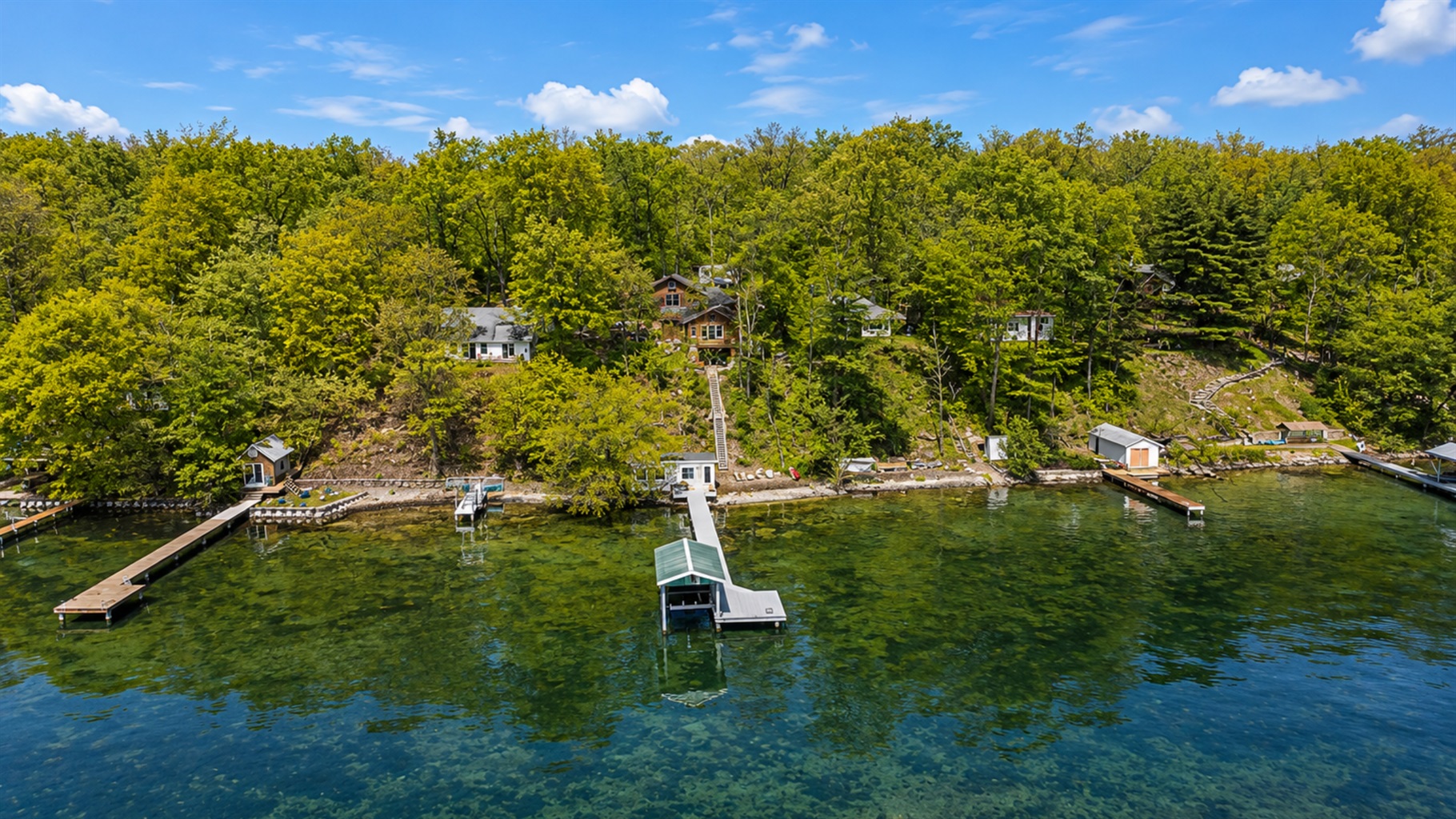 This stunning aerial view highlights a serene lakeside community, showcasing scattered cottages, lush greenery, and extensive docks for easy access to crystal-clear waters. An idyllic retreat for nature lovers.
