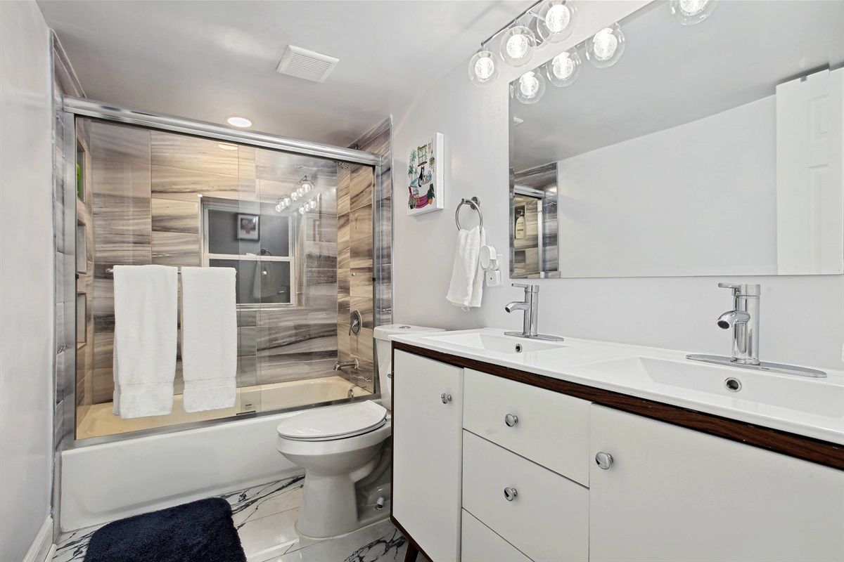 This full bathroom in the lower level has a tub with glass doors and a double vanity