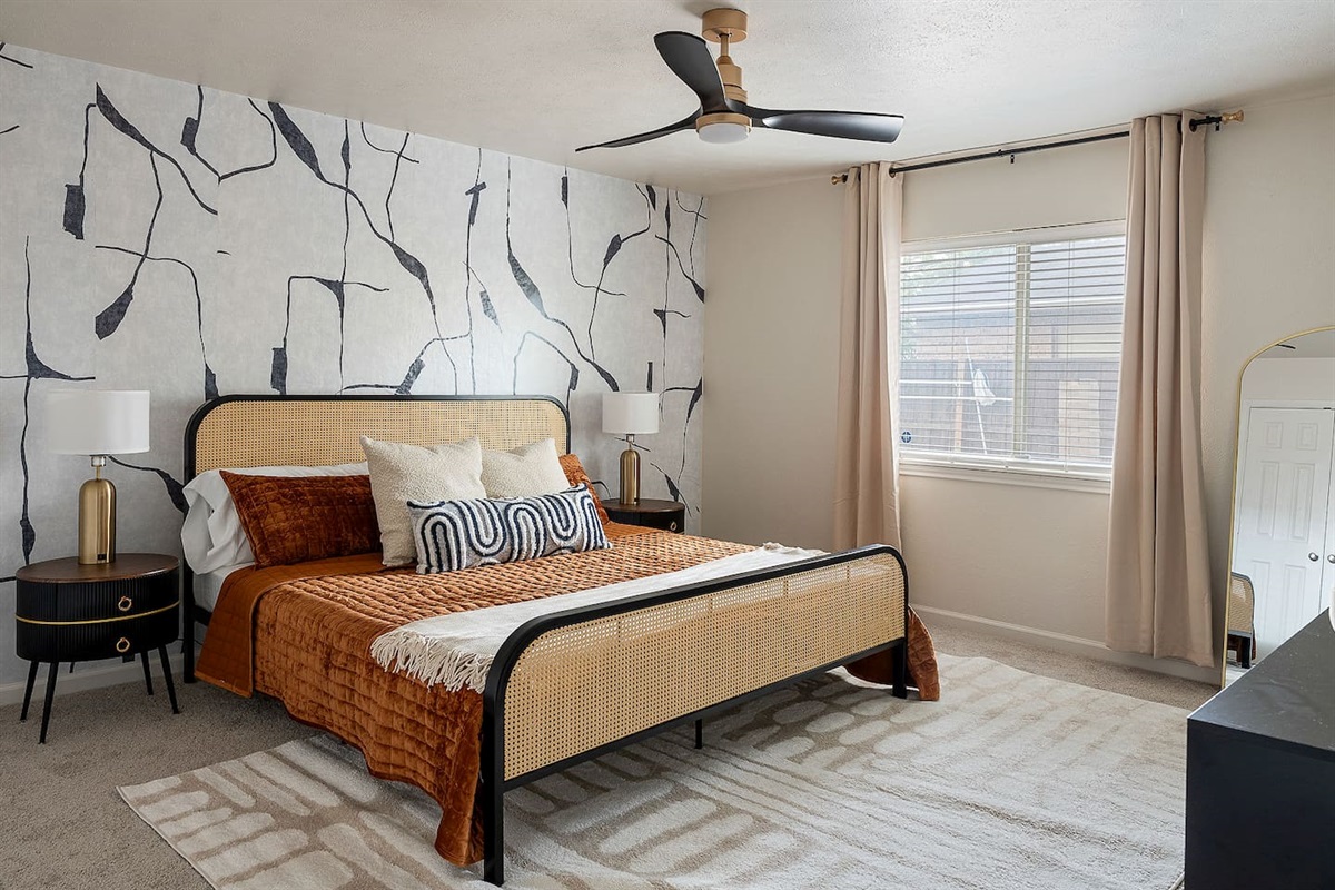 Relax in this stylish bedroom featuring a comfortable bed and unique wall decor. A ceiling fan ensures a pleasant atmosphere for a good night's sleep.