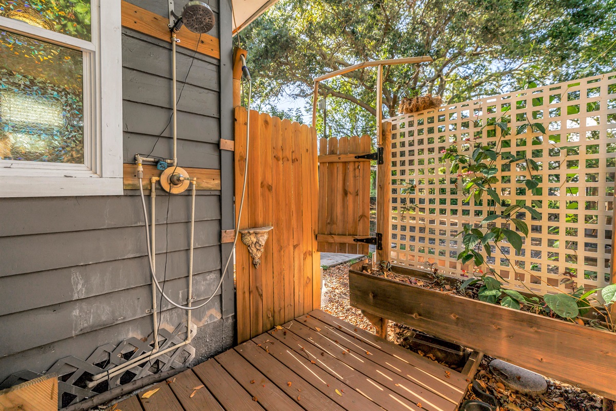 Private outdoor shower area with wood decking, lattice privacy screen, planter box, and a peaceful garden-style setting.