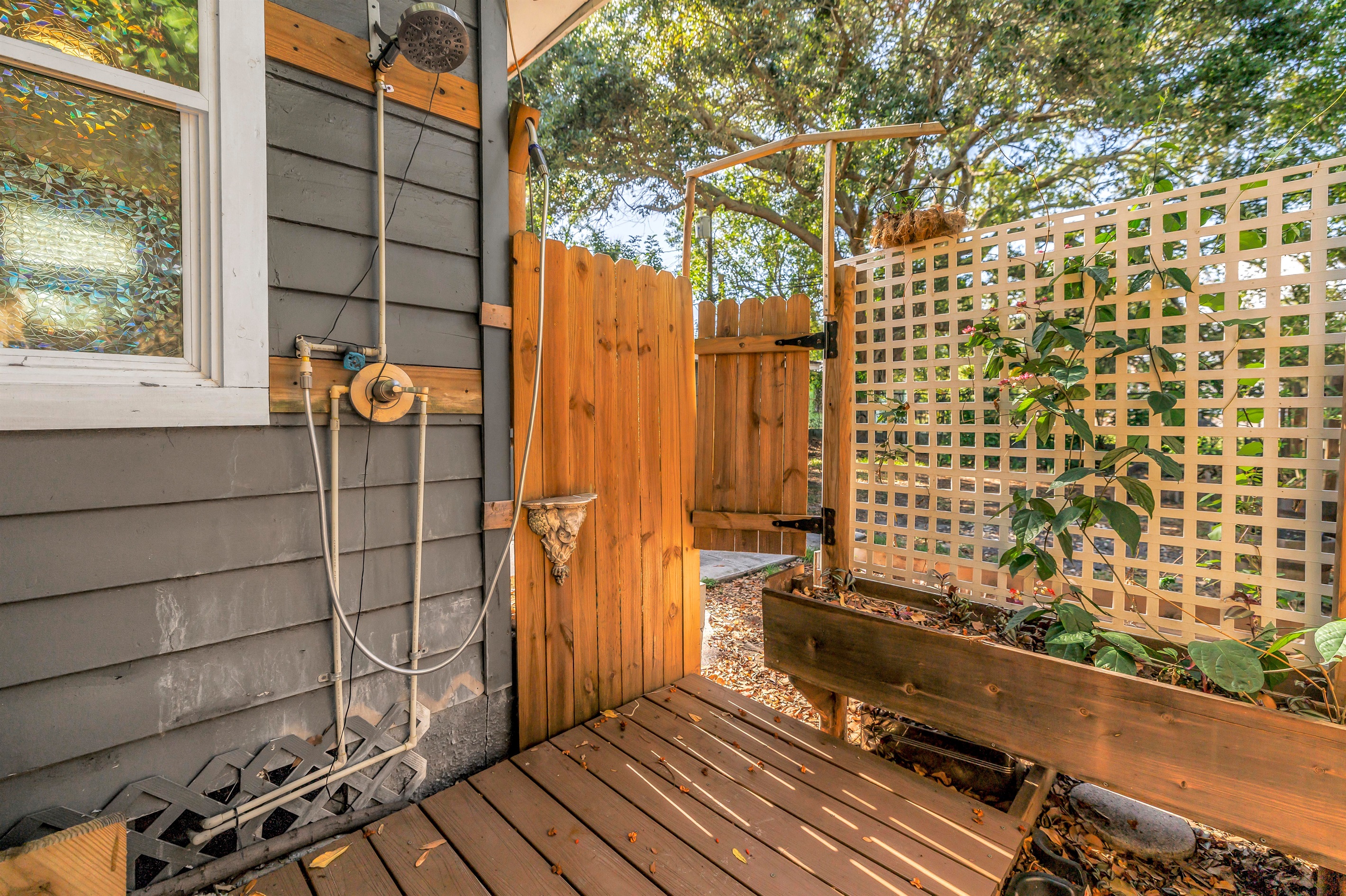 Private outdoor shower area with wood decking, lattice privacy screen, planter box, and a peaceful garden-style setting.