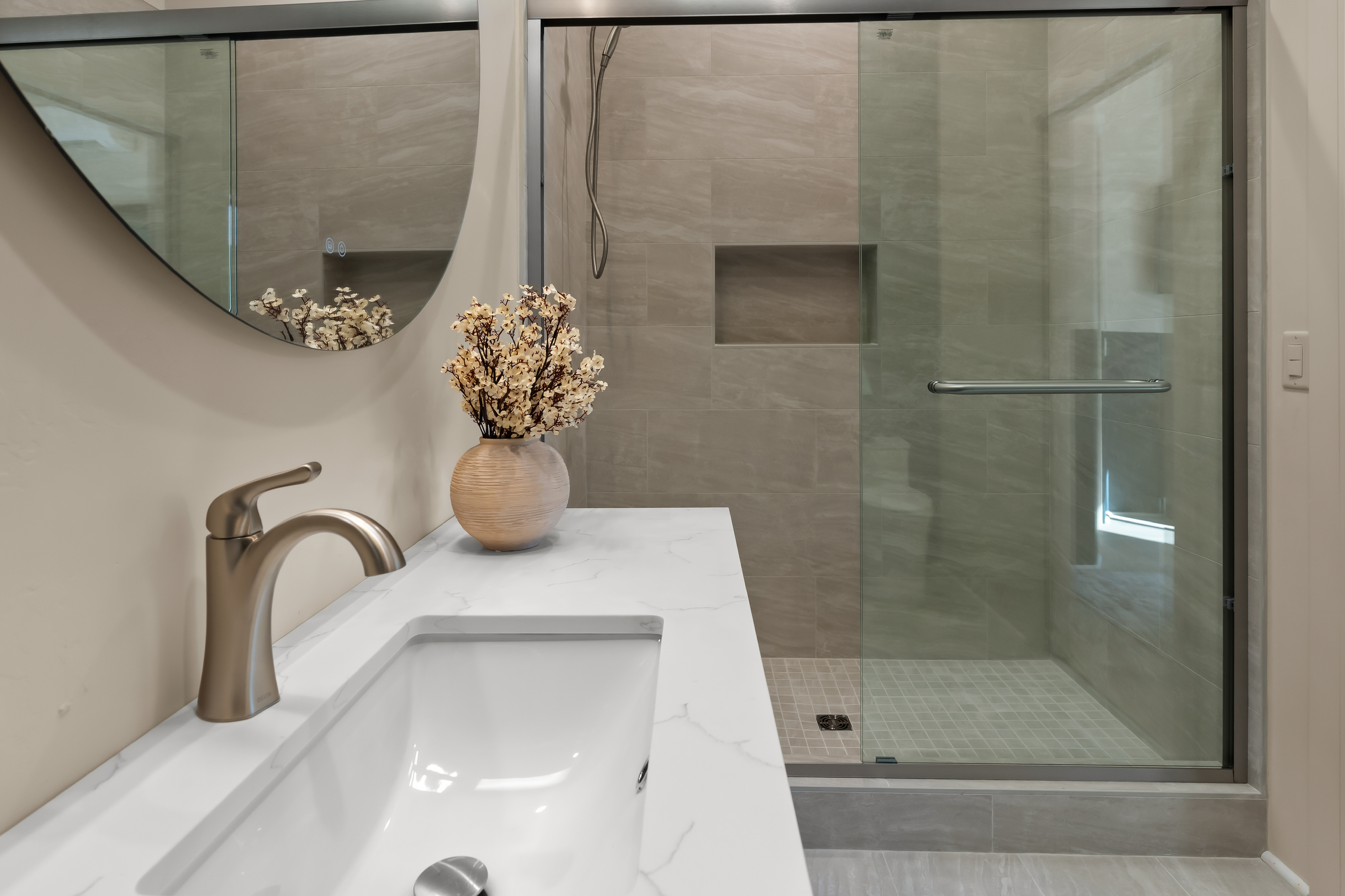 Spa-like walk-in shower with designer wall tiles and handheld wand, paired with a marble-veined quartz vanity top and brushed metal faucet.