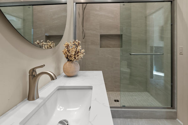 Spa-like walk-in shower with designer wall tiles and handheld wand, paired with a marble-veined quartz vanity top and brushed metal faucet.