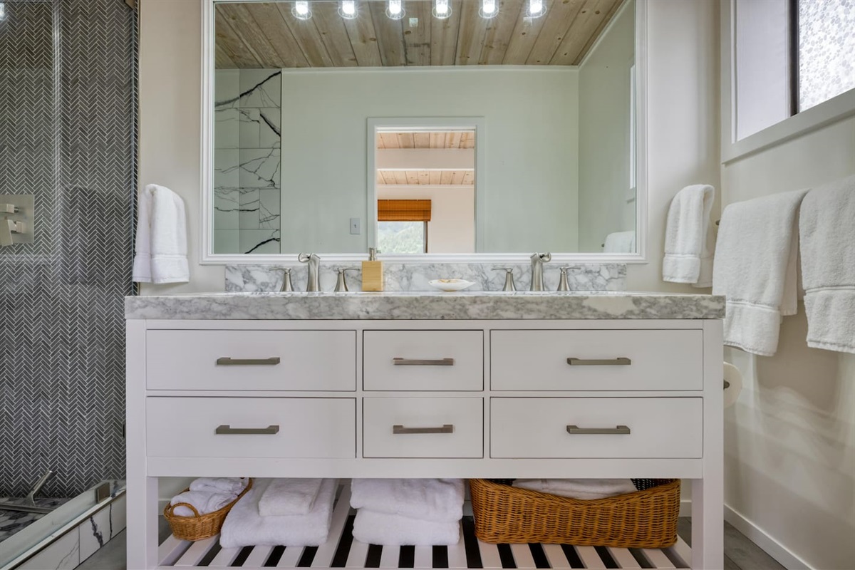 - Modern double vanity with marble countertop and plenty of drawer storage  
- Large mirror with bright vanity lighting for a well lit morning routine  
- Organized open shelf with baskets keeps towels and essentials within reach  
