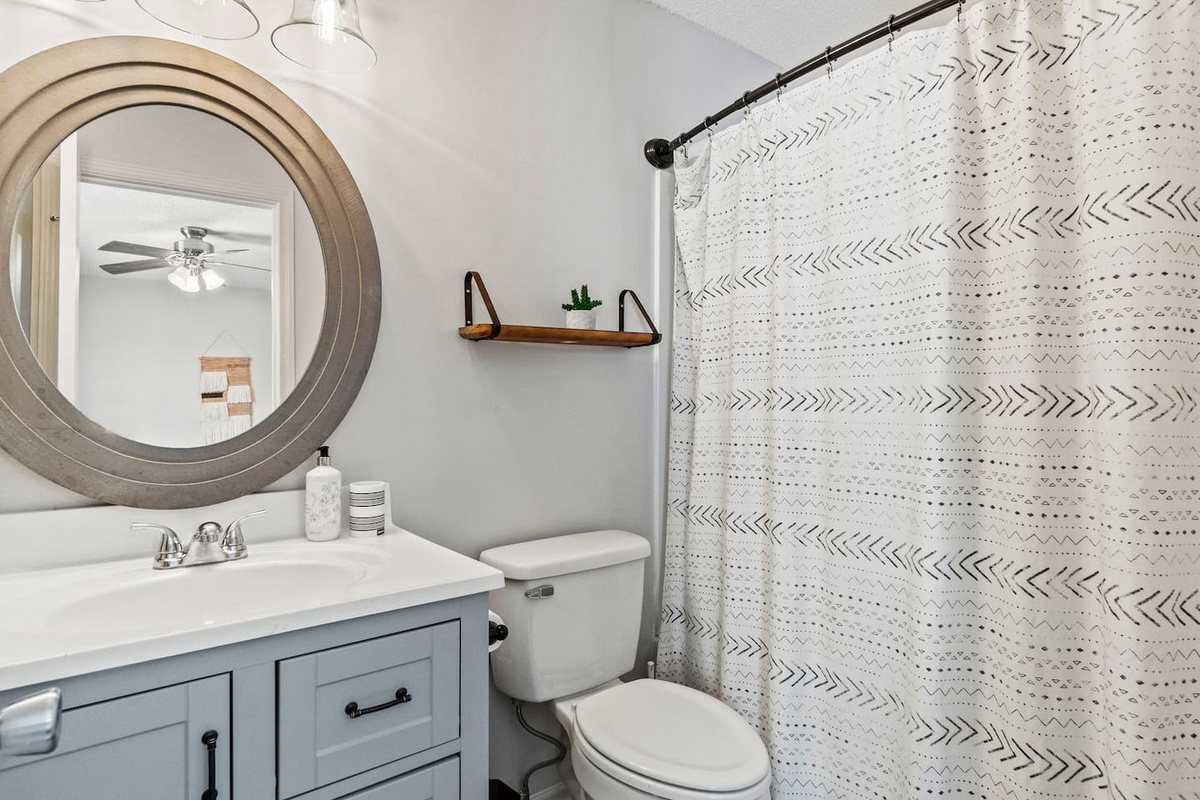 Bright and stylish bathroom featuring a soft-grey vanity, modern round mirror, and cheerful patterned shower curtain—complete with essentials for a fresh start to your day.