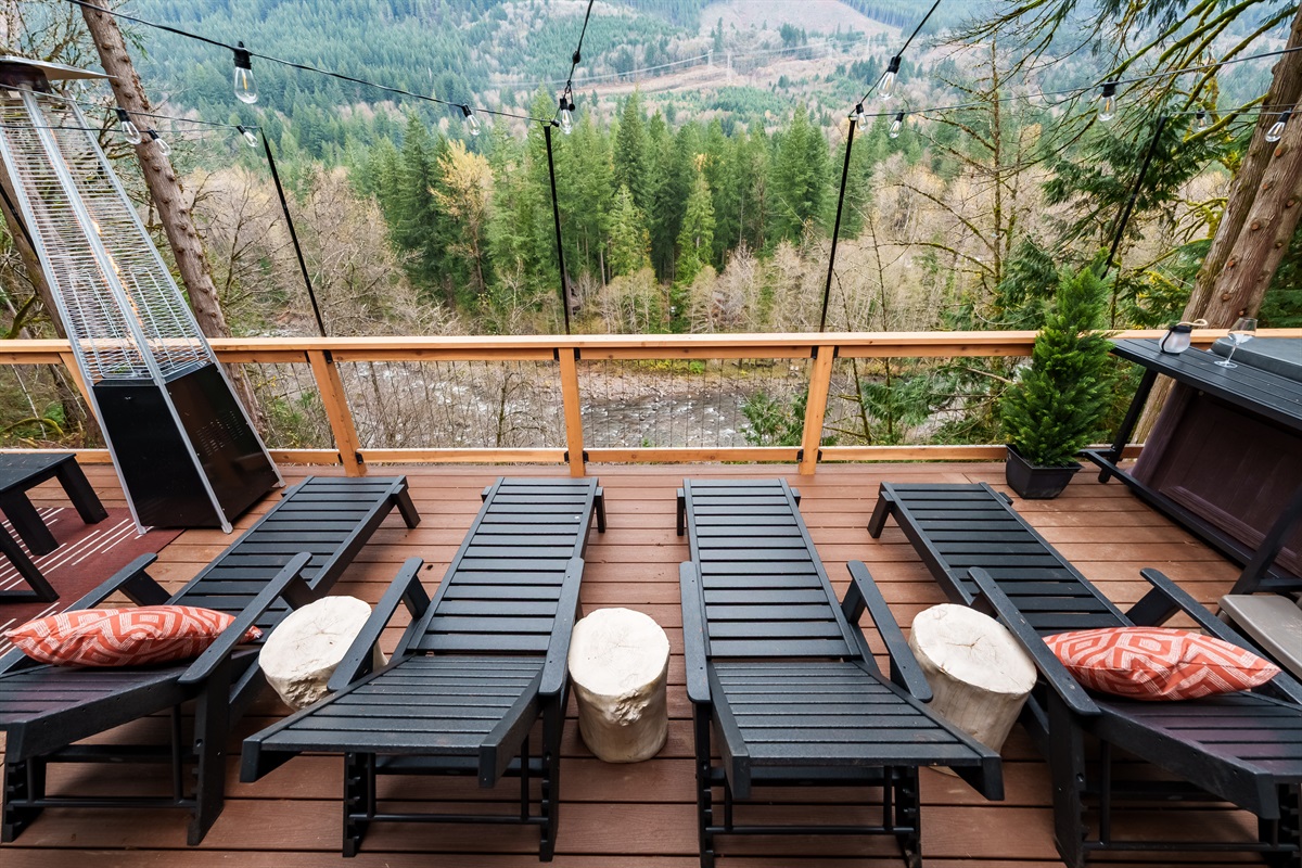 Unwind on the river-view lounge deck, where comfy chaise chairs, string lights, and towering evergreens create the perfect spot for morning coffee or sunset relaxation.