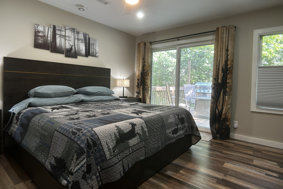 The king size bed has cotton sheets with high thread count. The room has dimmable lights, room darkening curtains and ceiling fan. Storage spaces include open shelving, dresser, side tables and closet space. Patio door leads to deck with hot tub.