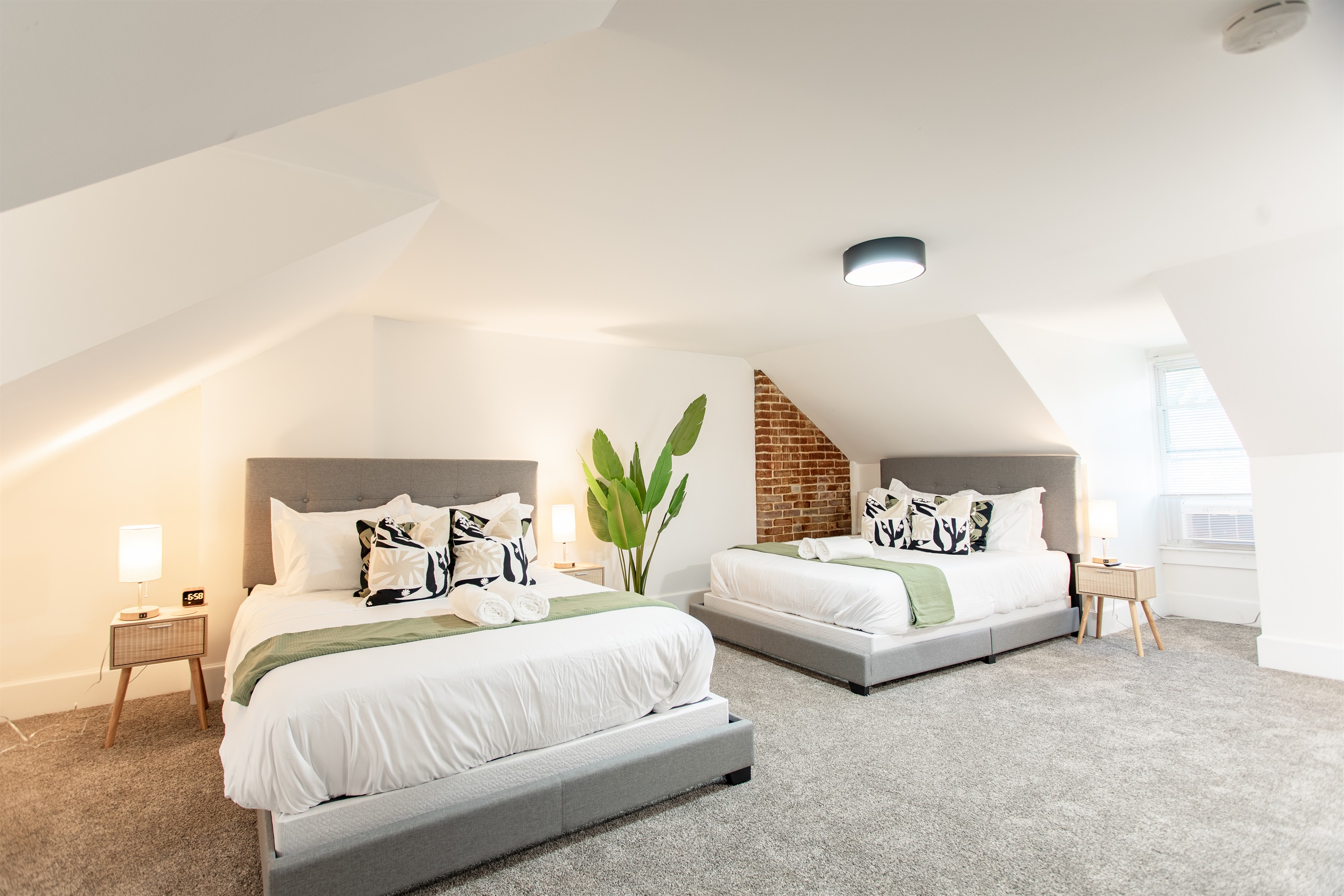 Spacious top-floor bedroom with two queen beds, modern décor, and exposed brick accents, complemented by a dedicated workspace for added convenience.