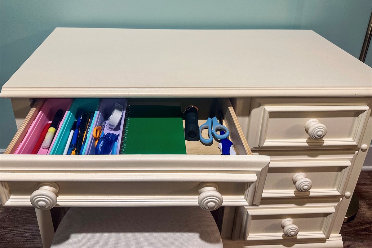 Desk drawer organized with office essentials including pens, pencils, scissors, and tape; additional drawers (not shown) include batteries, charging cables, and an extension cord.