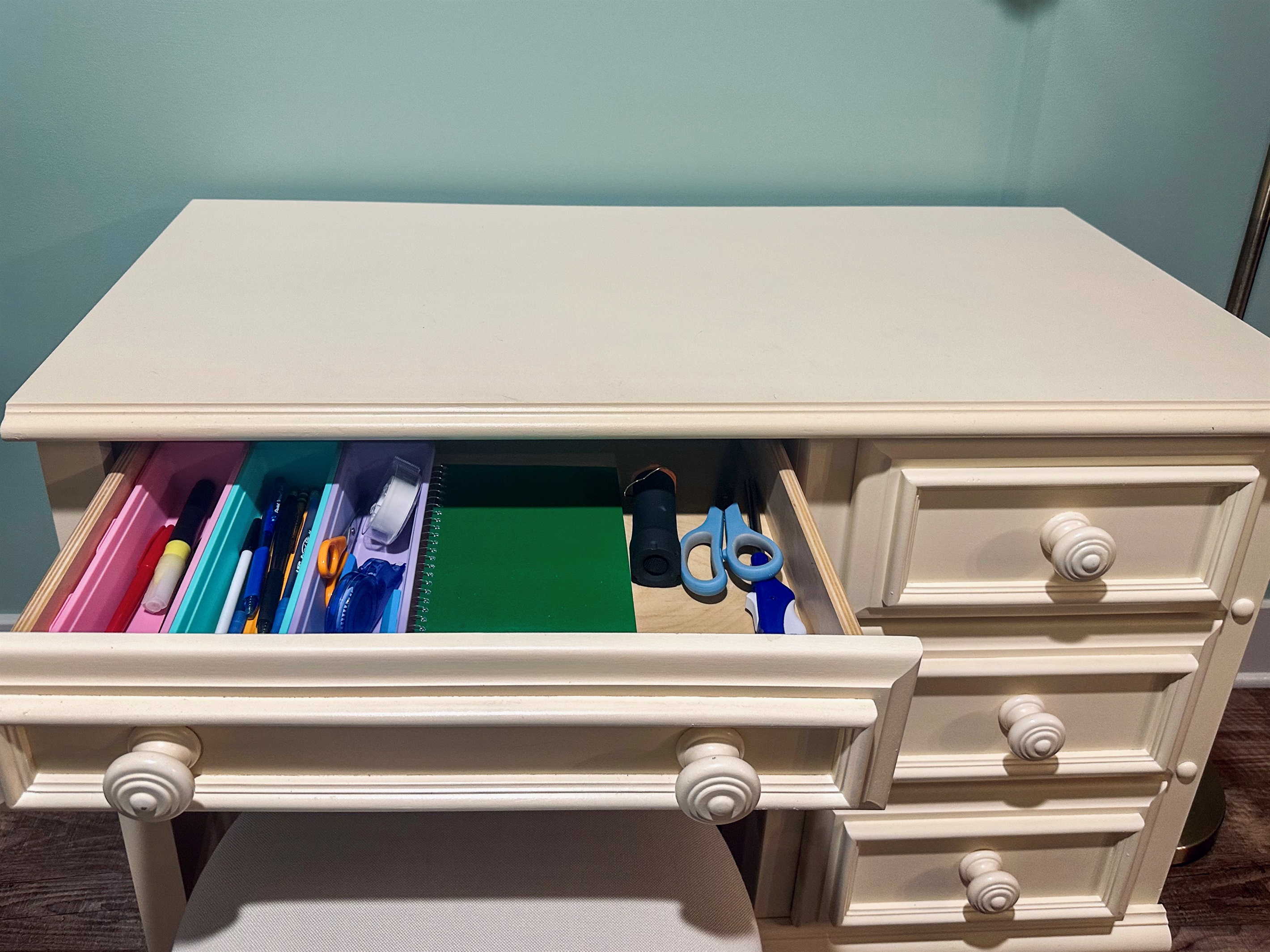 Desk drawer organized with office essentials including pens, pencils, scissors, and tape; additional drawers (not shown) include batteries, charging cables, and an extension cord.