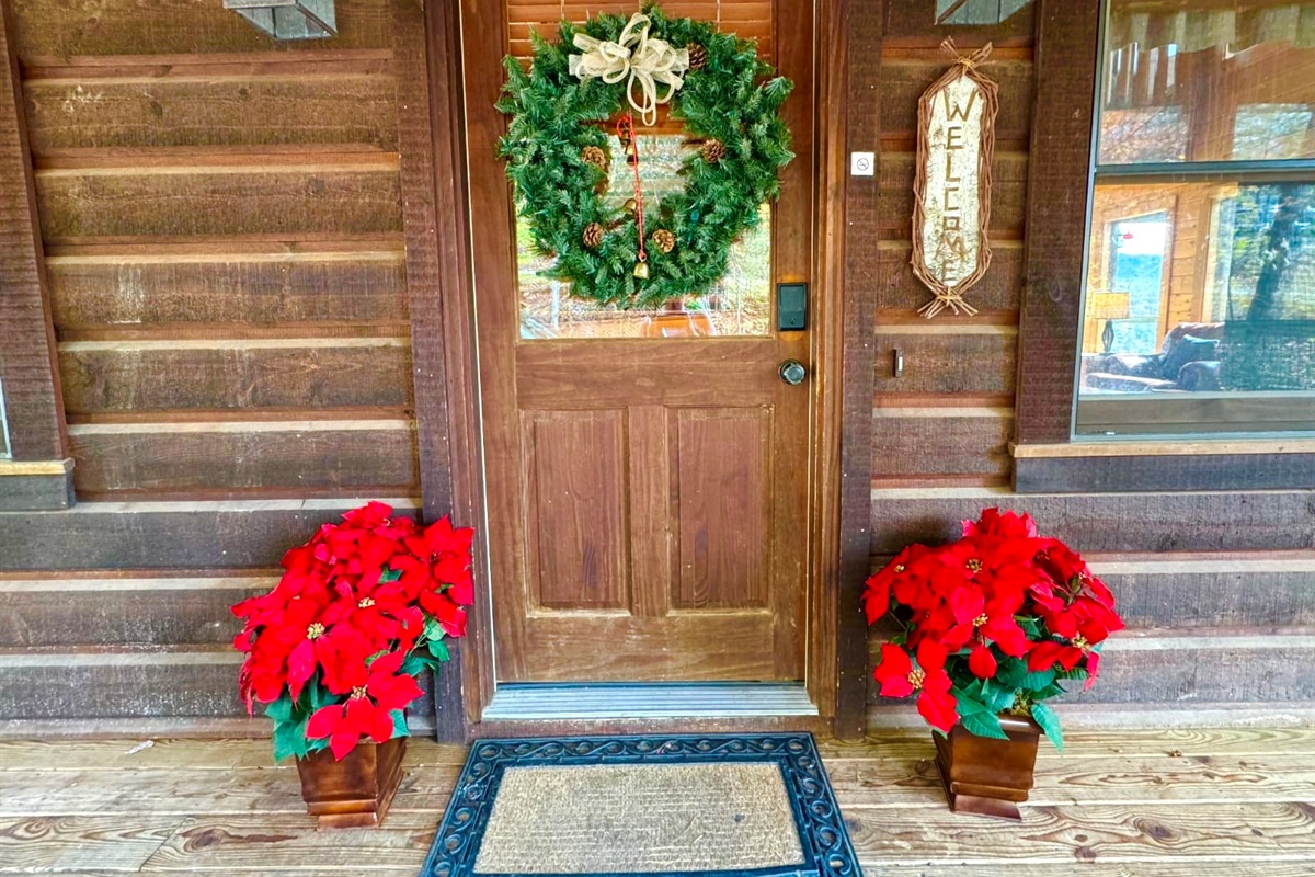 Step up to a charming “holiday welcome” a rustic wooden door framed by poinsettias and a pine wreath, setting the tone for a warm and cheerful stay inside.