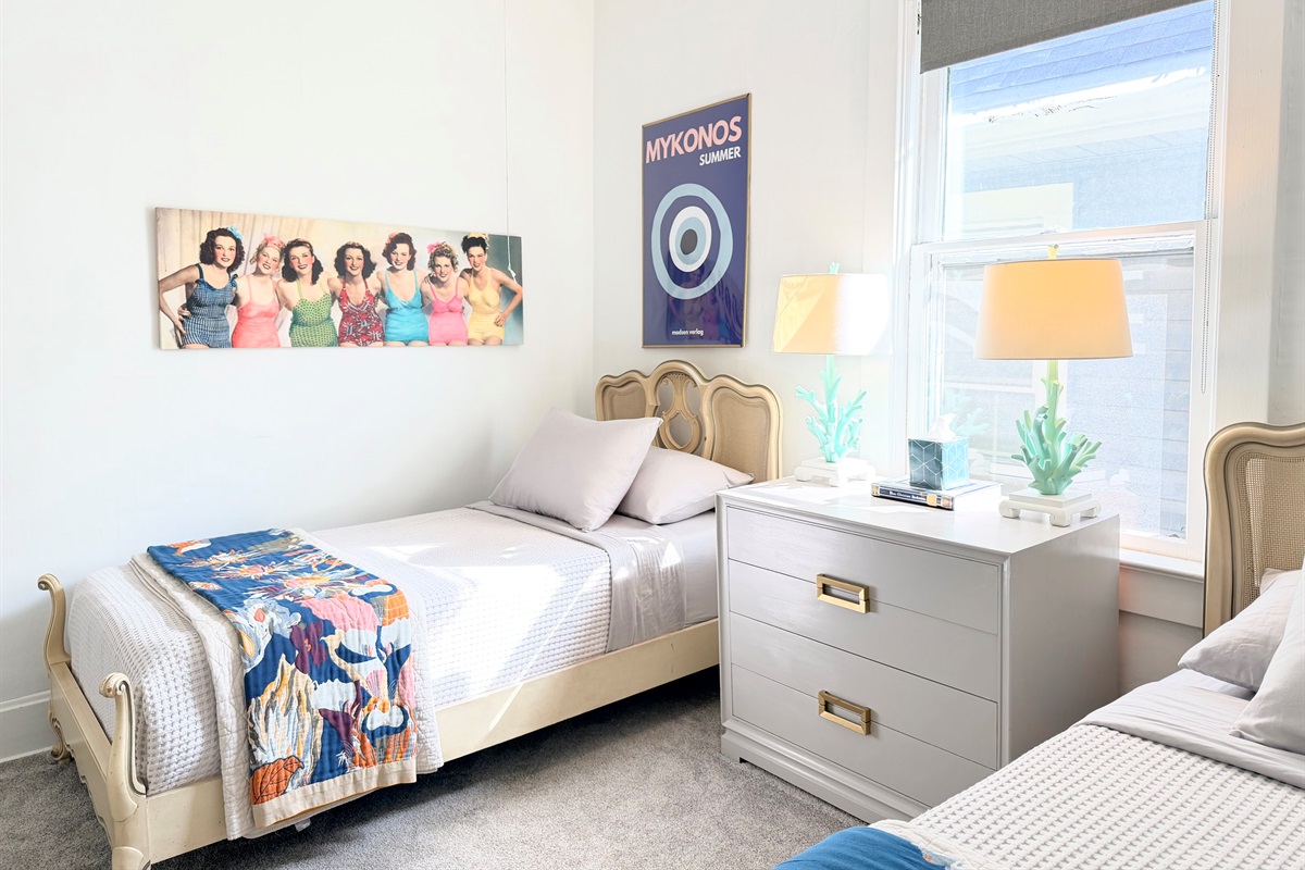 Two thoughtfully styled twin beds with supportive mattresses, crisp cotton linens, blackout shades, ceiling fan, and warm bedside lighting — a cozy, restful retreat for kids, friends, or shared stays.