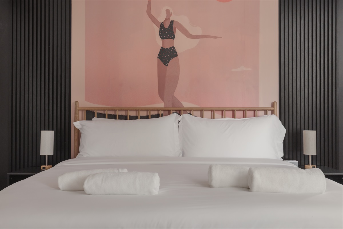 Drift off beneath a bold, beachy mural in this stylish king suite with crisp linens, calming tones, and curated design details.