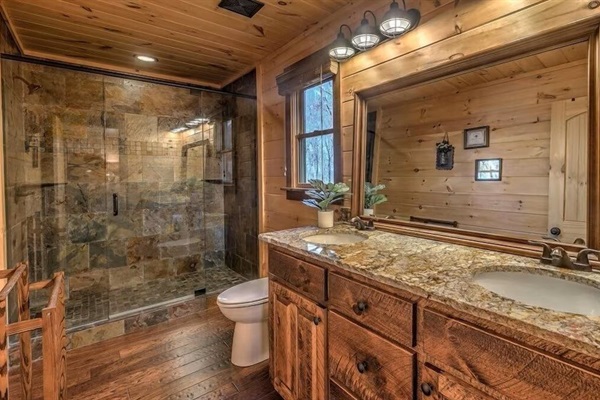 Guest bathroom featuring a walk-in stone shower, rustic wood vanity, and warm cabin finishes for a spa-like mountain experience.