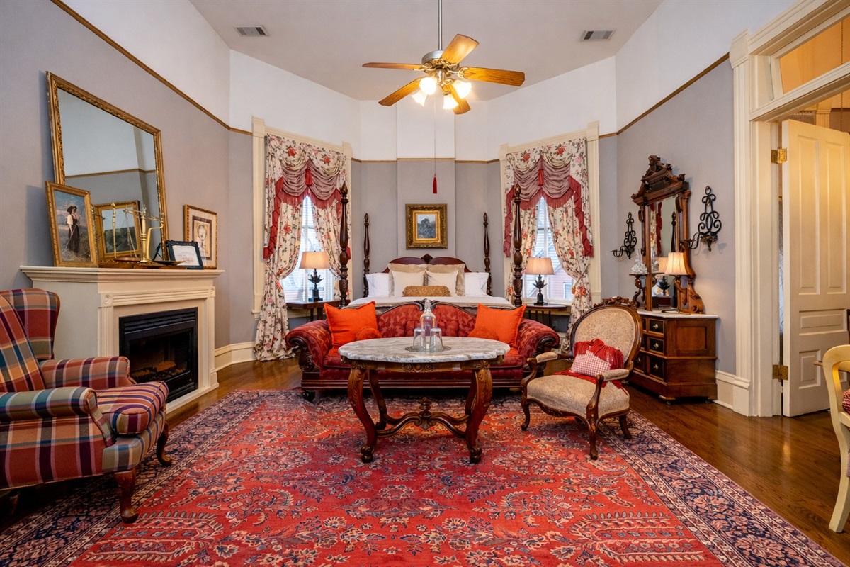 Victorian seating area with decorative fireplace, antique tables, and tall windows.  Washburn-Welch room at The Empress of Little Rock.