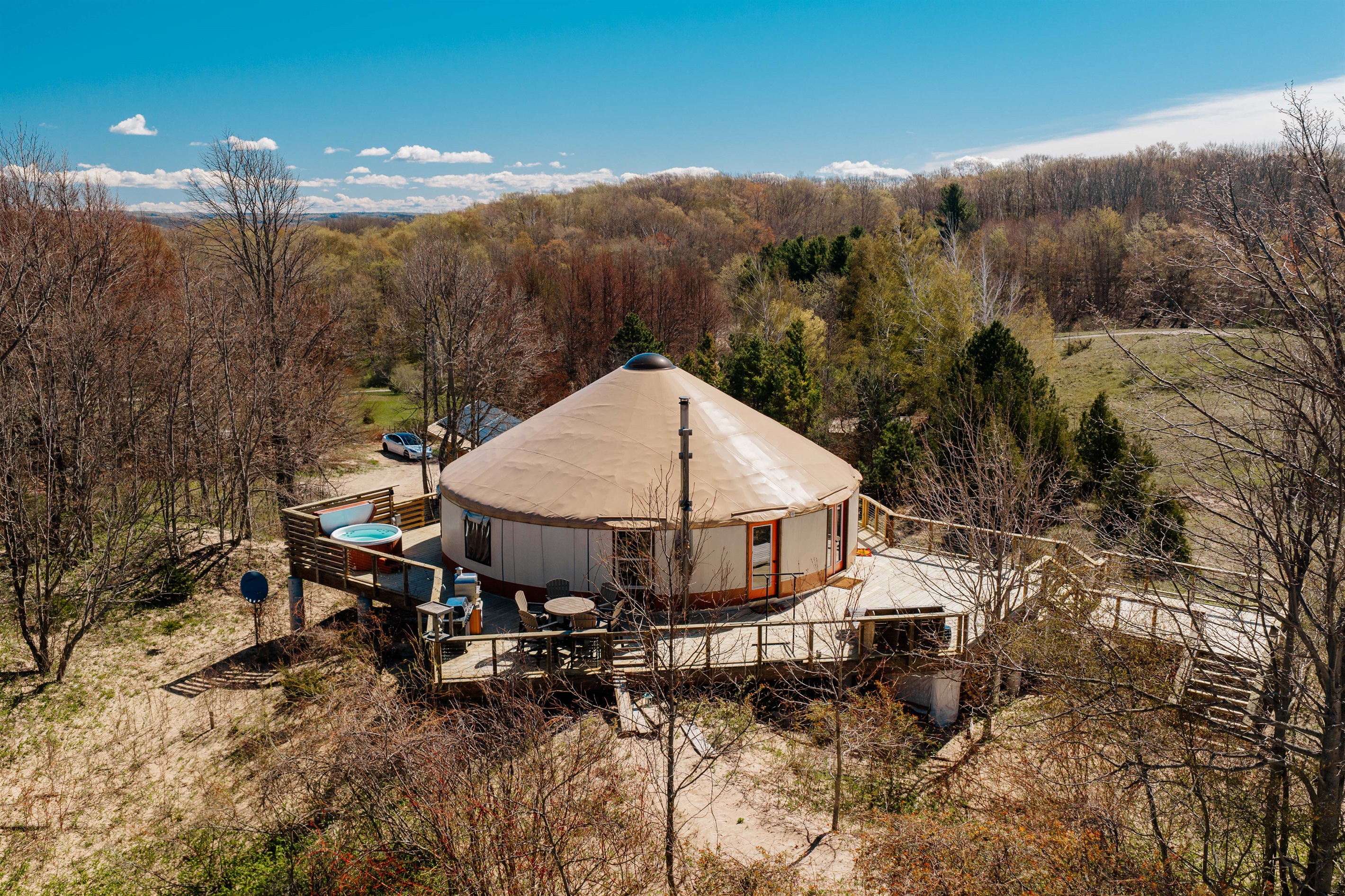 Wraparound decking surrounds the yurt, featuring outdoor dining, lounge areas, a hot tub, and peaceful dune-top views.