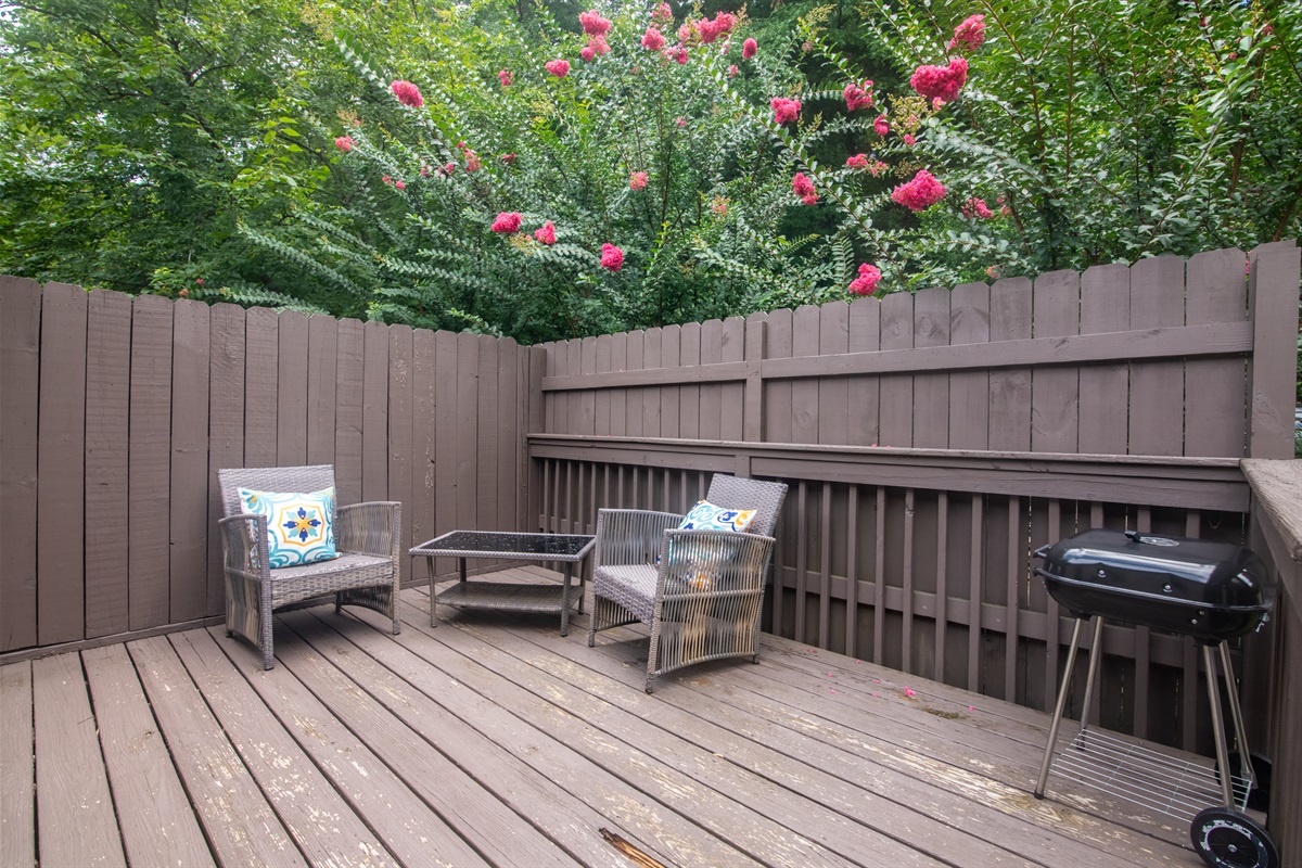 Relax and unwind on the outdoor space with seating and a grill surrounded by lush greenery.