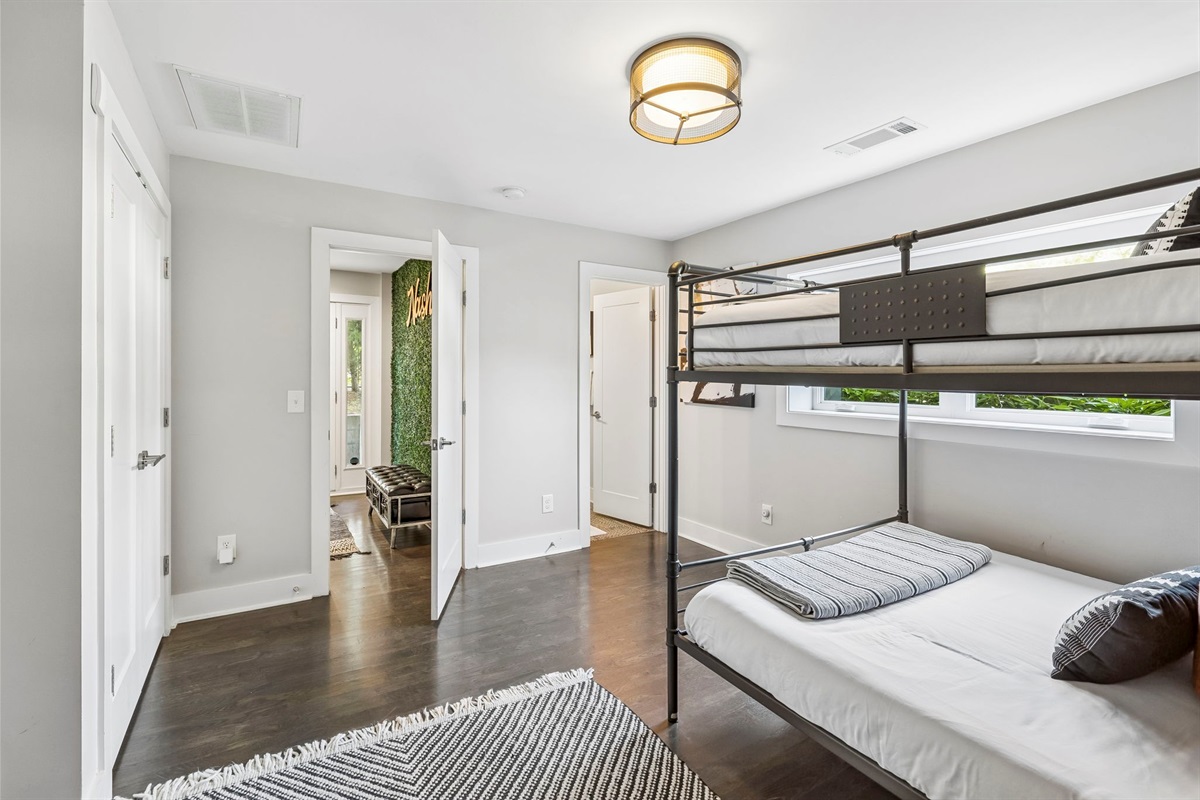 Stylish queen over queen bunk bed, dressed in modern striped linens - Includes a sleek desk, wall mounted TV, and tall mirror for comfort and convenience - Monochrome rug and minimalist d&eacute;cor create a polished, cozy sleep and work space