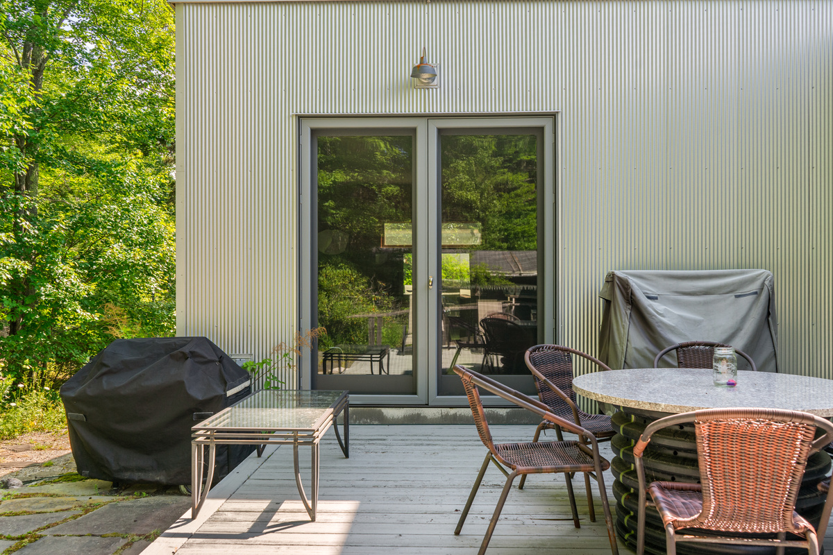 Outdoor living at "The Crag." The spacious deck features outdoor dining seating, a covered grill, and direct glass door access to the primary bedroom suite—all backed directly by the trees of Acadia National Park.