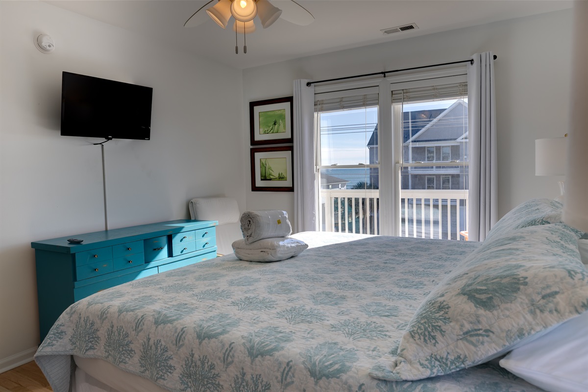 A King-size bed with coastal bedding, smart TV, dresser, ceiling fan, and plenty of natural light in Upstairs master