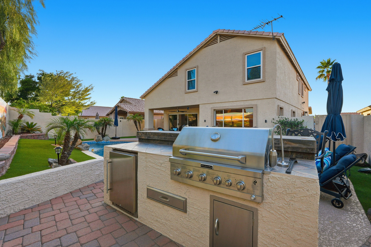 Outdoor built-in BBQ area with grill, counter space, pool views, and easy access to the backyard lounge seating.