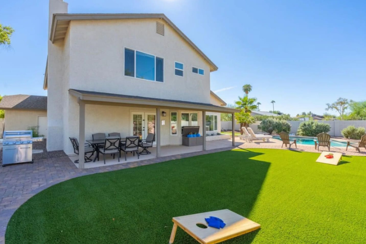Modern home with expansive lawn, covered patio, outdoor kitchen, and sparkling pool—perfect for entertaining and games.