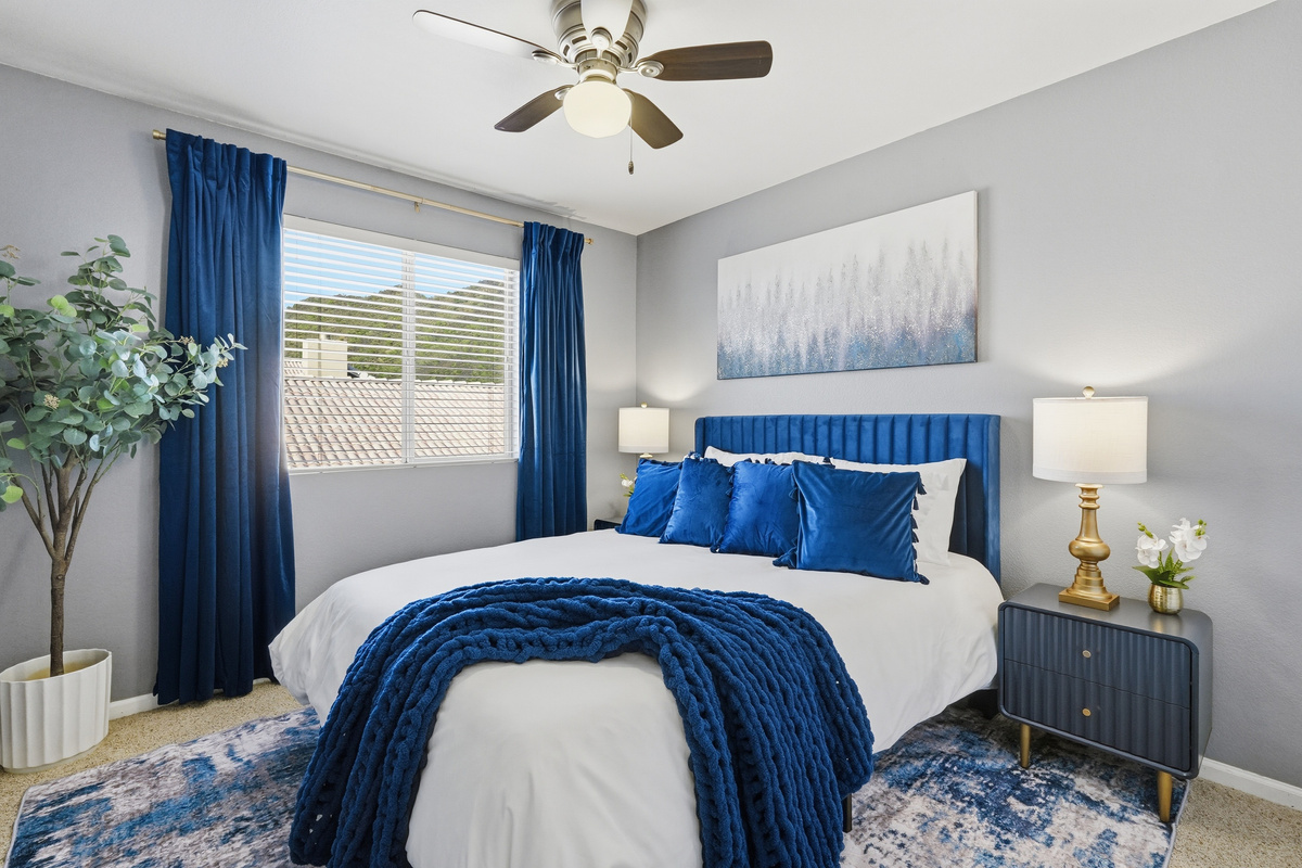 Bedroom with blue accent styling, ceiling fan, bedside lighting, and a calm setup for a comfortable stay.