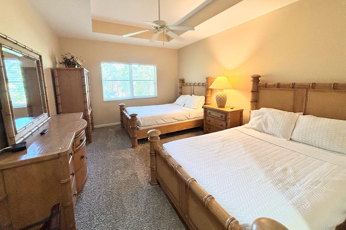 Spacious bedroom featuring two comfortable beds, tray ceiling with ceiling fan, cozy seating area, and plenty of natural light.