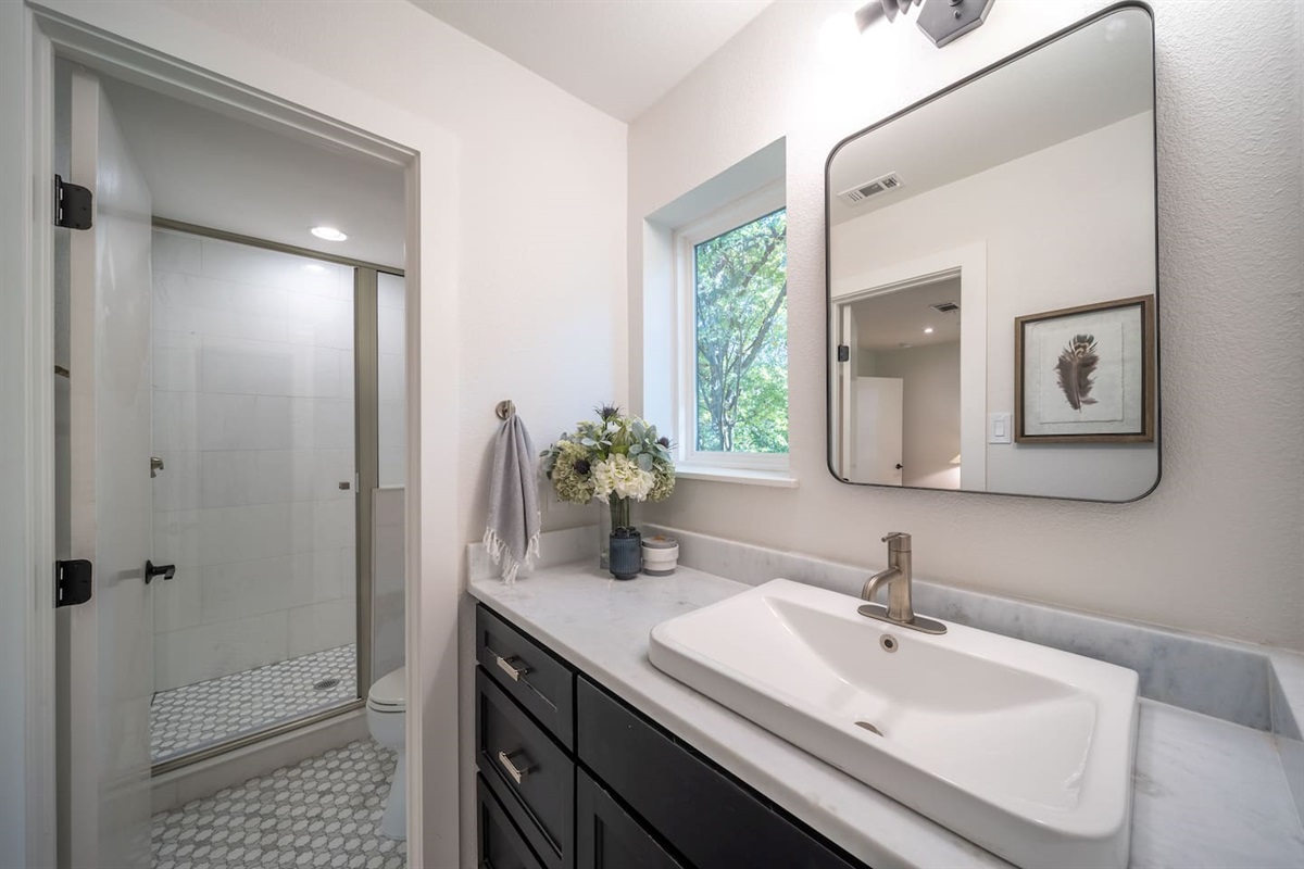 A full view of the Bedroom 2 ensuite bathroom showcases the walk-in shower, marble surfaces, and contemporary design elements. The space feels bright, fresh, and quietly luxurious. You'll have access to shampoo, conditioner, bodywash, and hand soap. 