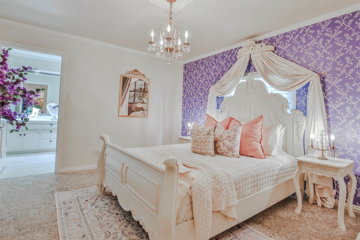 The Wisteria Room: Where dreams bloom beneath wisteria walls and chandelier glow. A queen bed, fireplace, smart TV, and Jack and Jill bath complete this floral retreat.