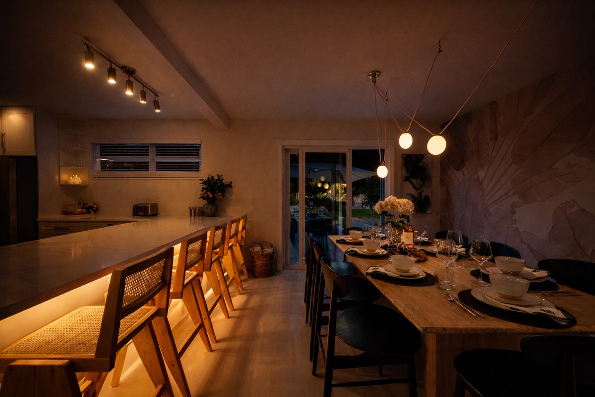 Designer dining room featuring a Gwyneth Paltrow GOOP statement light, custom wallpaper, and seating for 12. Backlit counter seating and seamless access to the patio and backyard make this space ideal for family meals and entertaining.