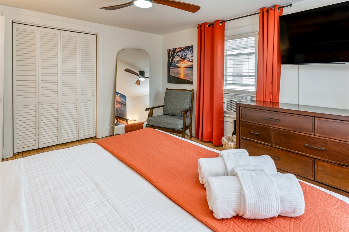Spacious king bedroom with vibrant orange accents, smart TV, and lots of natural light for a cozy, modern retreat. Bedroom #1 upstairs 