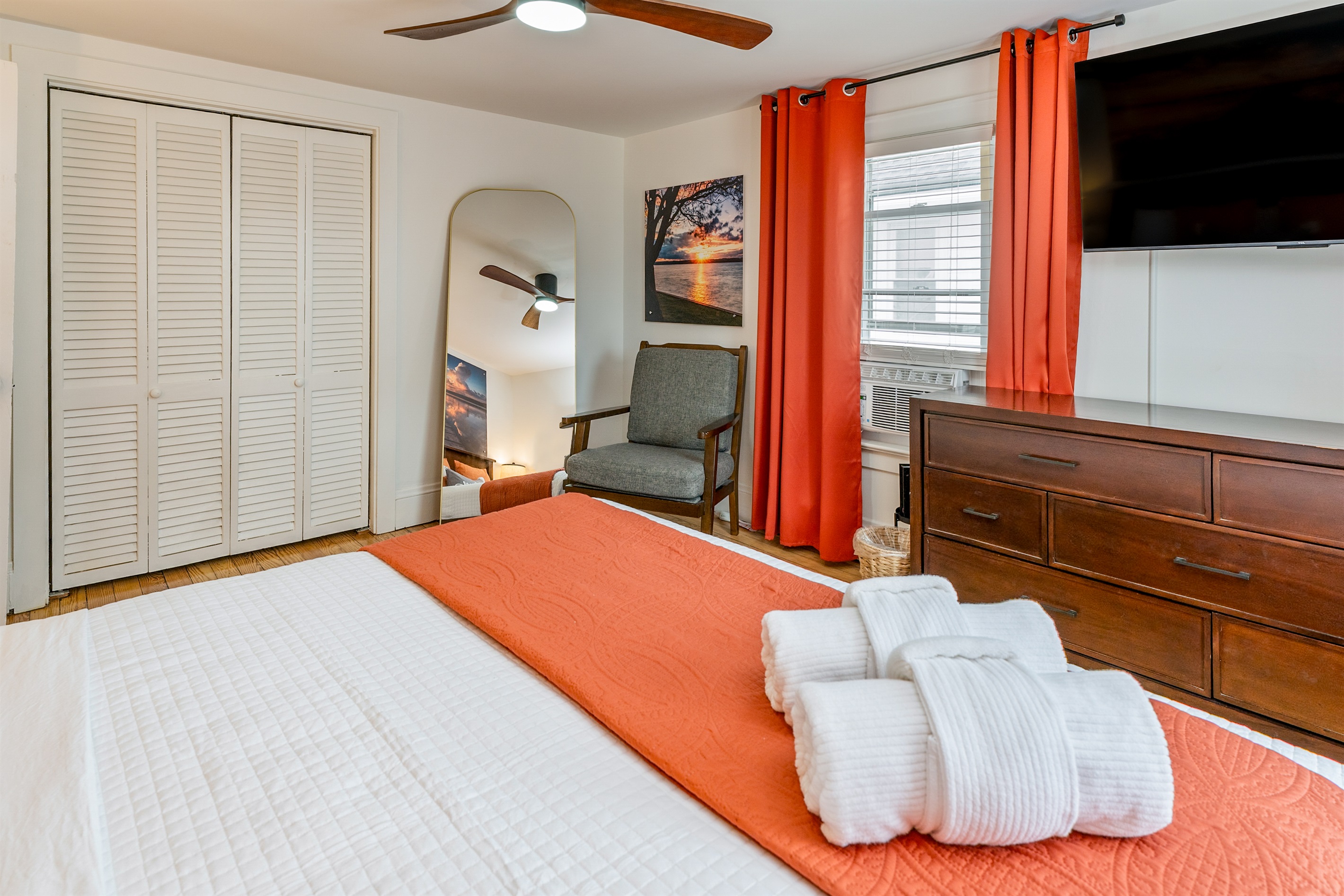 Spacious king bedroom with vibrant orange accents, smart TV, and lots of natural light for a cozy, modern retreat. Bedroom #1 upstairs 