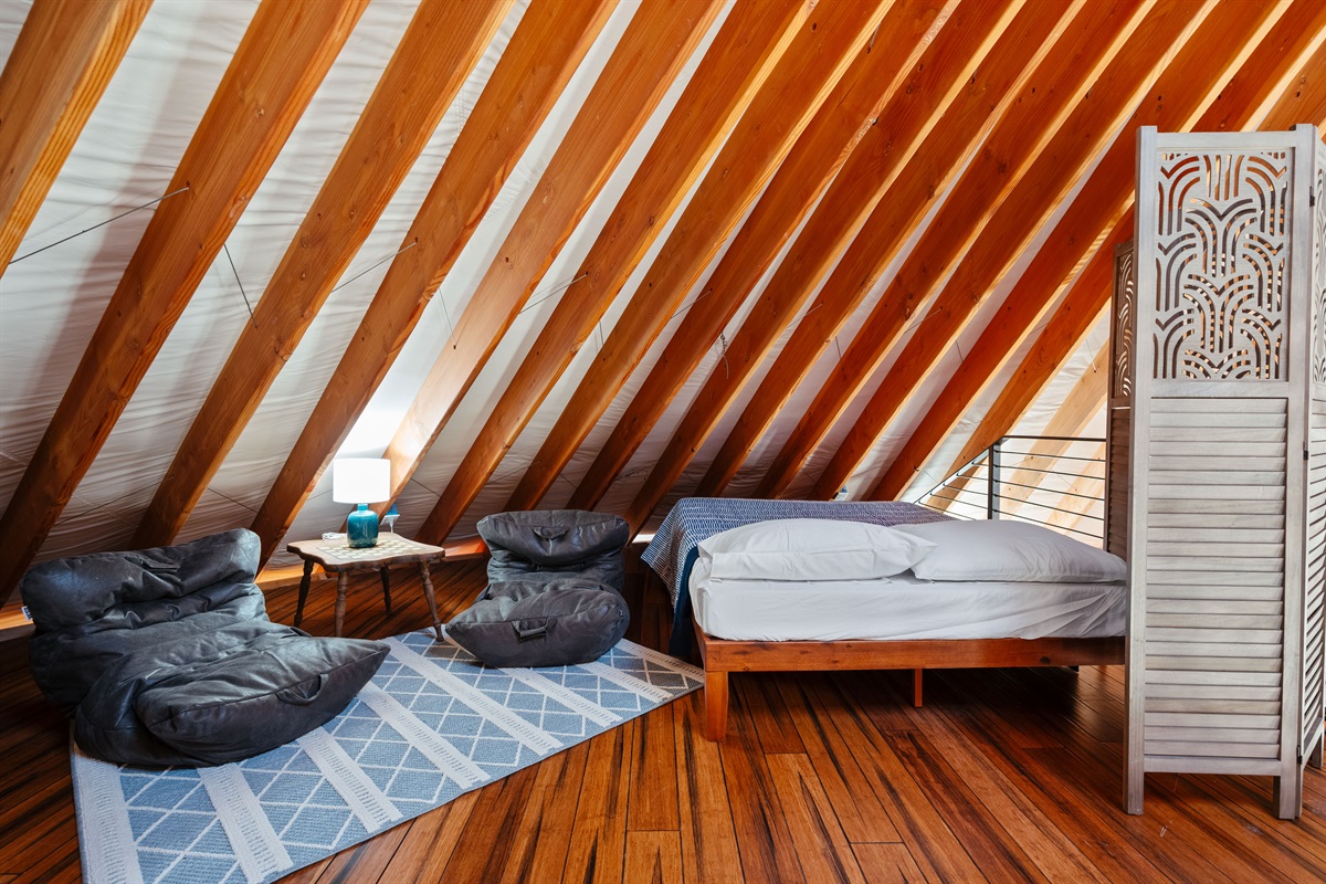 Open loft sleeping area featuring two full beds with privacy dividers, cozy seating, and elevated views overlooking the main living space below.