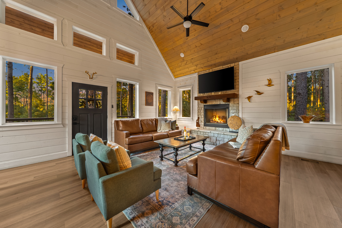 Soaring wood ceilings, walls of windows, and a cozy stone fireplace create a gathering space that feels both elevated and inviting.