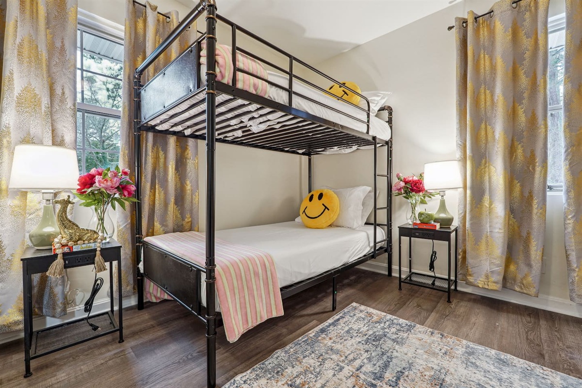 A cozy bedroom featuring a double bed, a bunk bed, a window, a bedside shelf with a lamp, and a TV — perfect for families or groups to relax and unwind.
