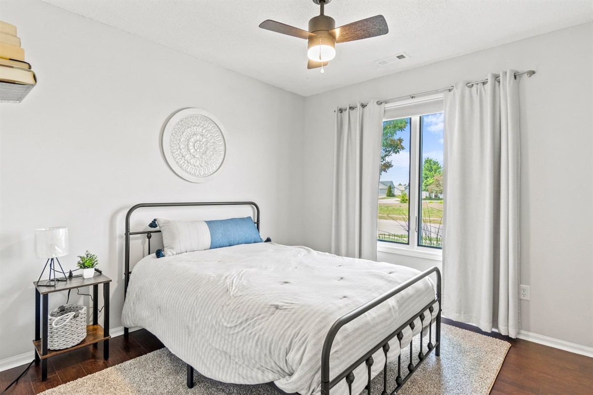 This bright and airy bedroom features a full-size bed with crisp white linens and a blue lumbar pillow, creating a calm and cozy retreat.
