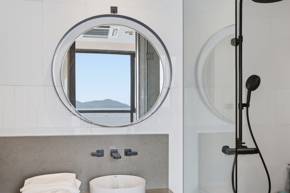 Bathroom with round mirror, concrete vanity, black fixtures, and shower with mountain water view visible through window.