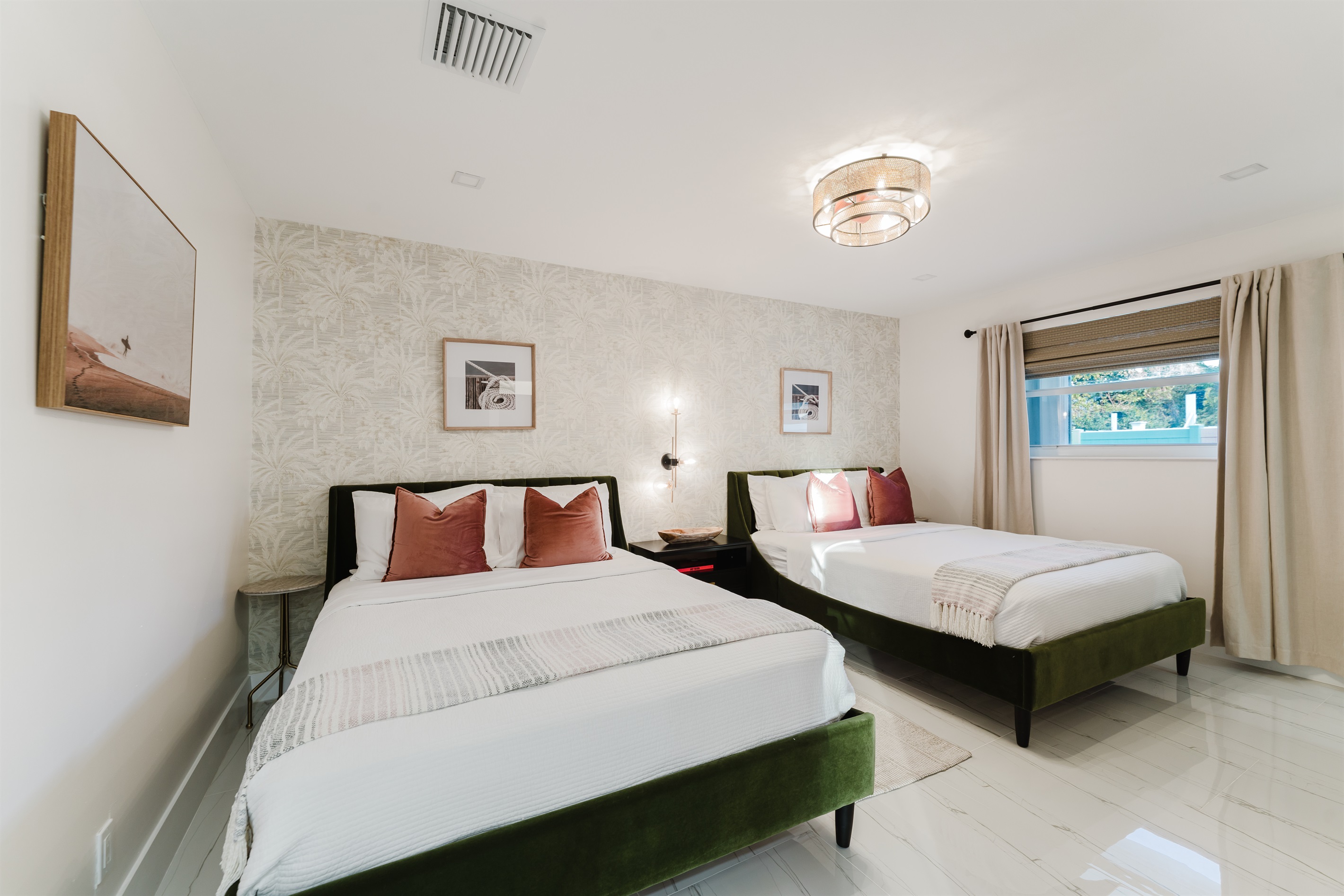 Bright coastal suite with two queen beds, private ensuite bath, smart TV, blackout bamboo shades, and a rattan ceiling fan—ideal for families or shared stays.